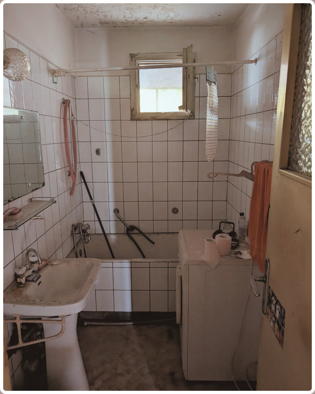 Baie veche cu tencuială căzută, faianță albă cu rosturi și prosop portocaliu — înainte de renovare