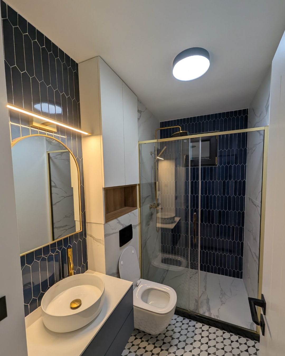 Baie renovată cu plăci hexagonale navy, finisaje aurii și gresie geometrică alb-negru — după renovare
